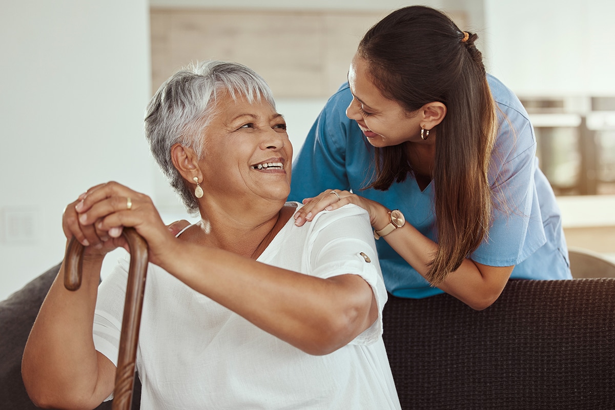 senior woman with caregiver smile while sitting on a living room sofa